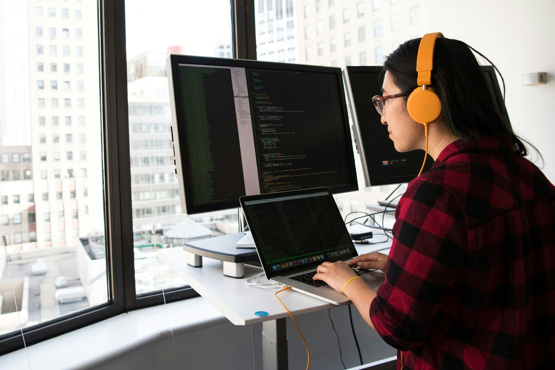 A programmer working on code on a laptop beside a desktop monitor in an office - Kimi K3.1 Pro