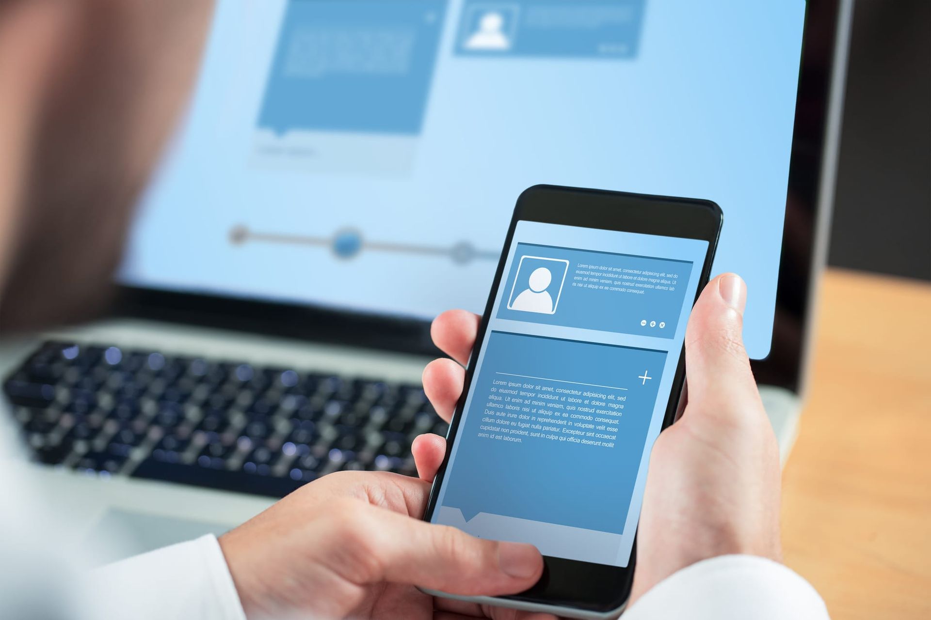 Hands using a smartphone next to a laptop on a wooden desk - remove personal information from the internet