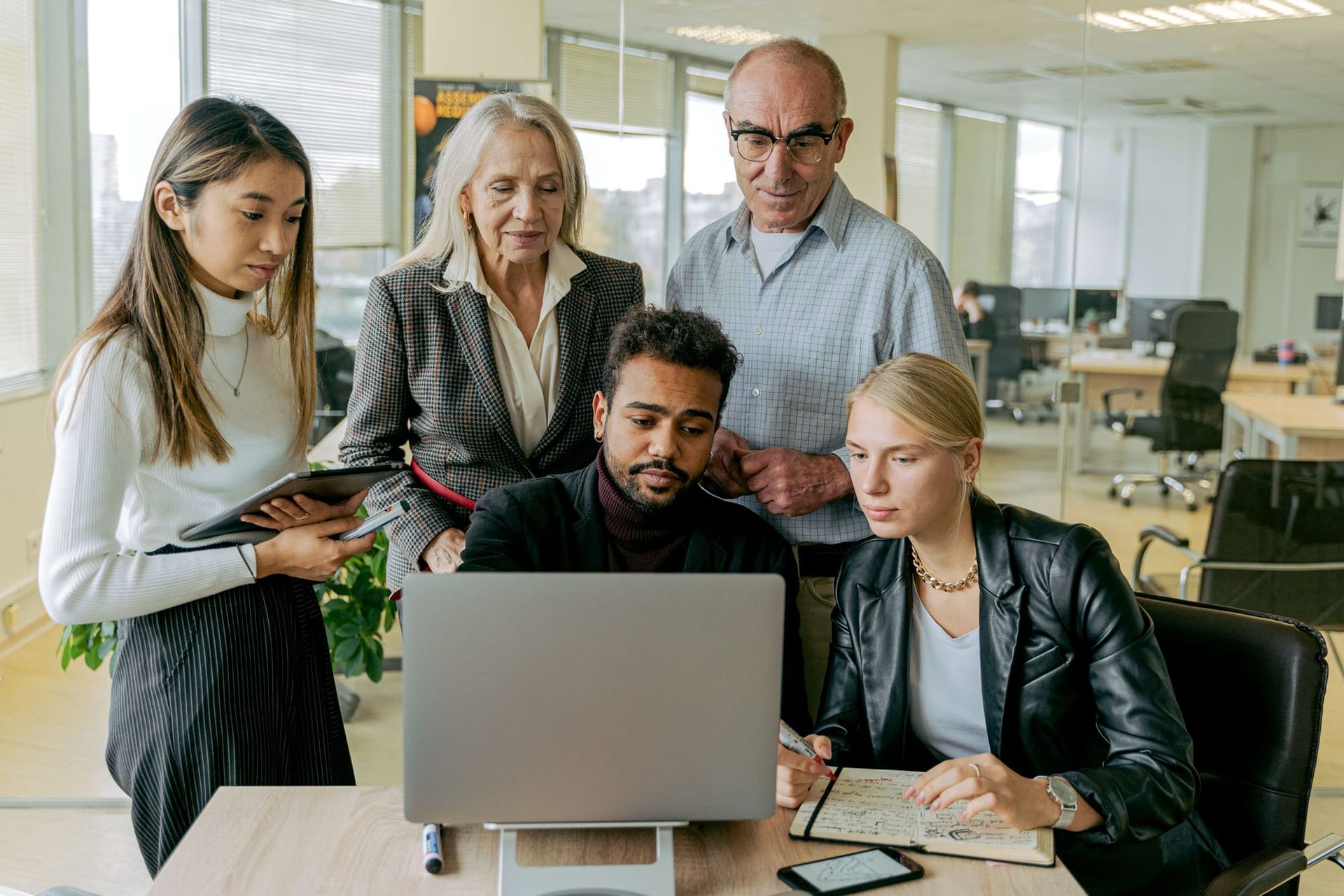 Five colleagues gathered around a laptop during an office meeting - AI ROI