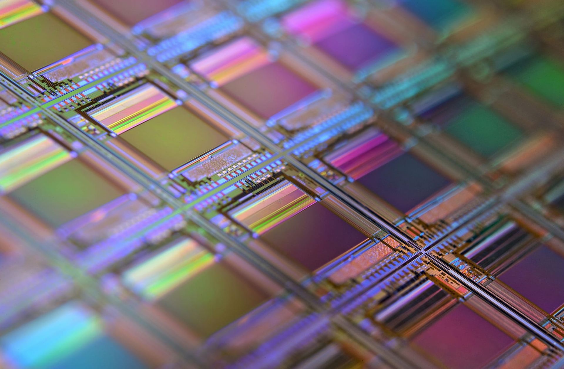 Close-up of a silicon wafer showing an iridescent grid of microscopic semiconductor circuits.