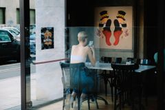 Woman sitting in a café and looking at her smartphone through a window - Bumble acquisition