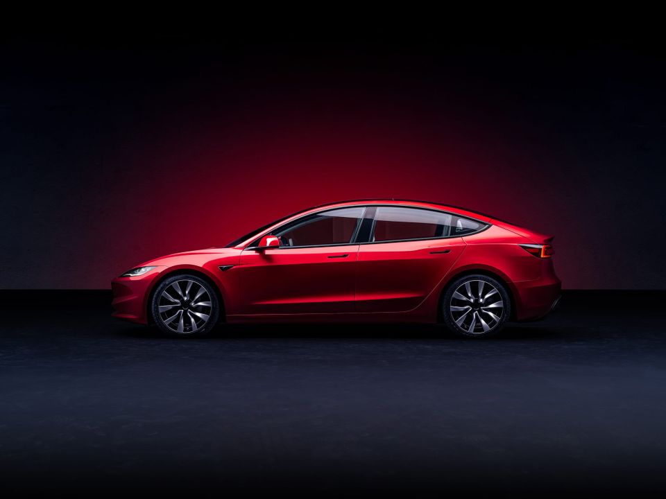 Red Tesla electric sedan photographed in profile against a dark studio background with red accent lighting - Tesla Full Self-Driving claims
