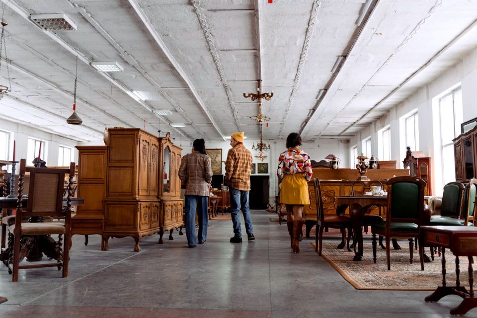 Three shoppers walking among wooden tables, cabinets and chairs inside a furniture store - October 2026 consumer sentiment