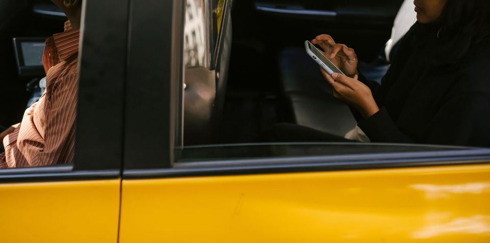Passenger looking at a smartphone while riding in the back seat of a yellow taxi - FTC personalized pricing inquiry