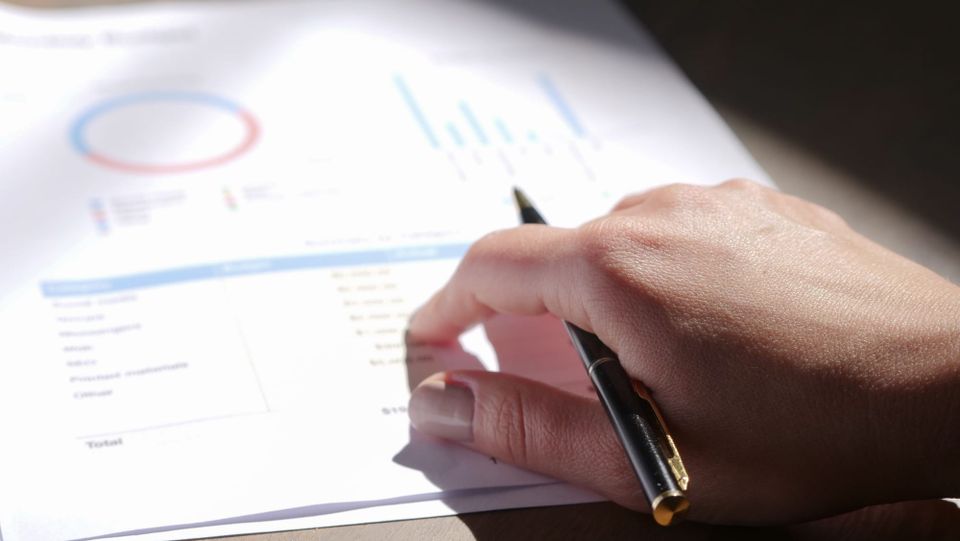 A hand holding a pen over a financial worksheet on a desk - Anthropic public benefit fund