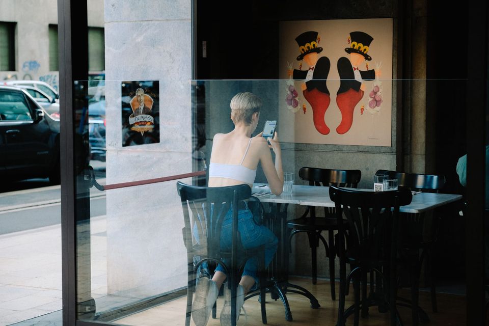Woman sitting in a café and looking at her smartphone through a window - Bumble acquisition