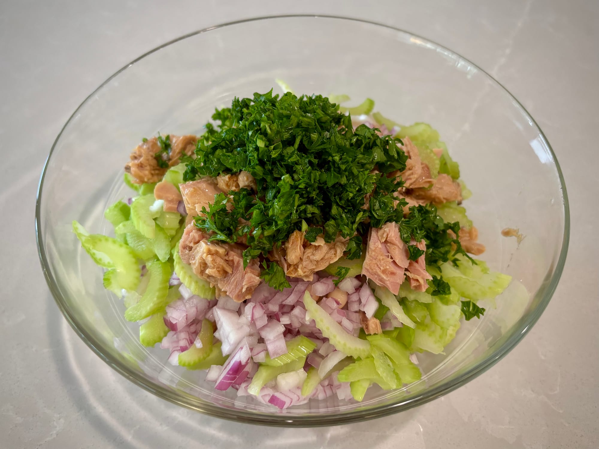 Beans, onions, celery, tuna and parsley in a glass bowl