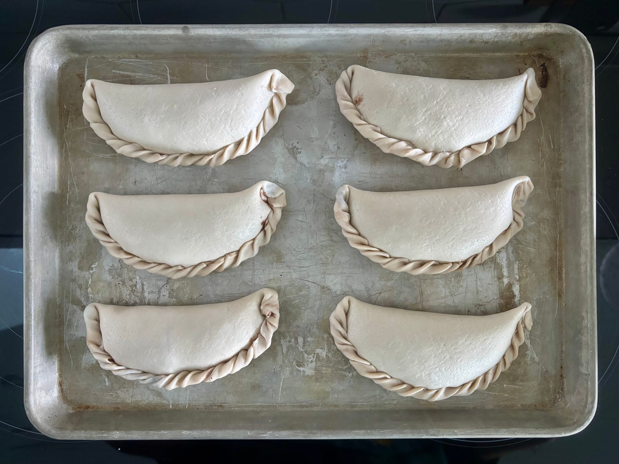 Six uncooked empanadas on a sheet pan