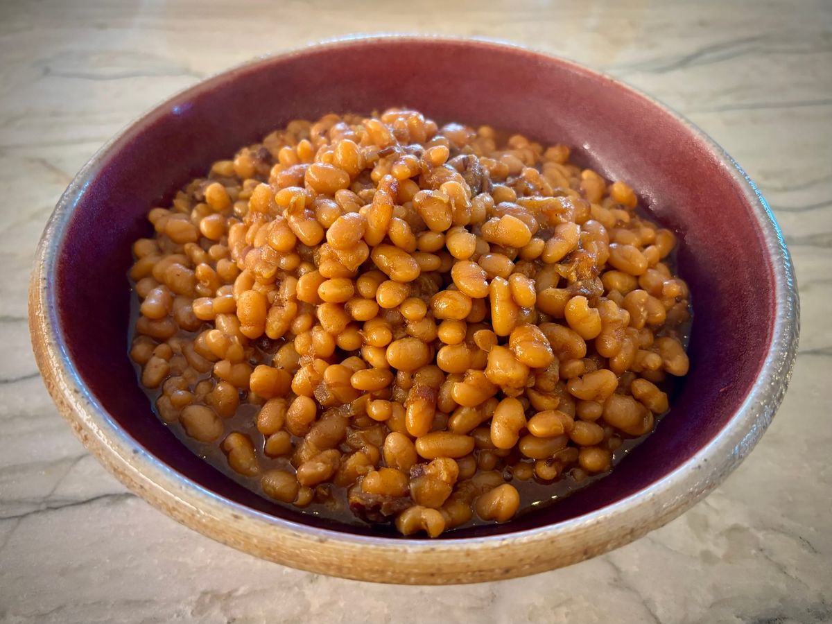A red glazed ceramic bowl filled with baked beans