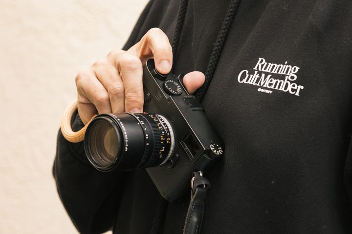 Person holding Leica M10 Monochrom while wearing a Satisfy Running Cult Member hoodie