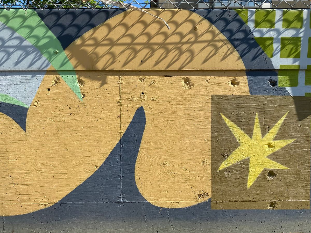 Outdoor mural of geometric shapes with shadows of a chainlink fence.