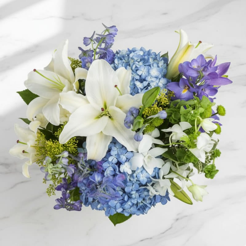 Luxury birthday flower arrangement with white lilies, blue hydrangea, and purple orchids from Grace & Blooms Naples. Sculptural design perfect for milestone celebrations.