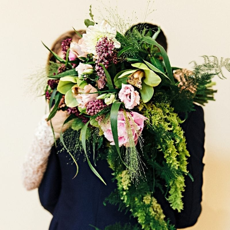 A couple at their Naples wedding embrace behind a large, custom Tropical Chic bouquet of heat-resistant green orchids designed by a local florist.