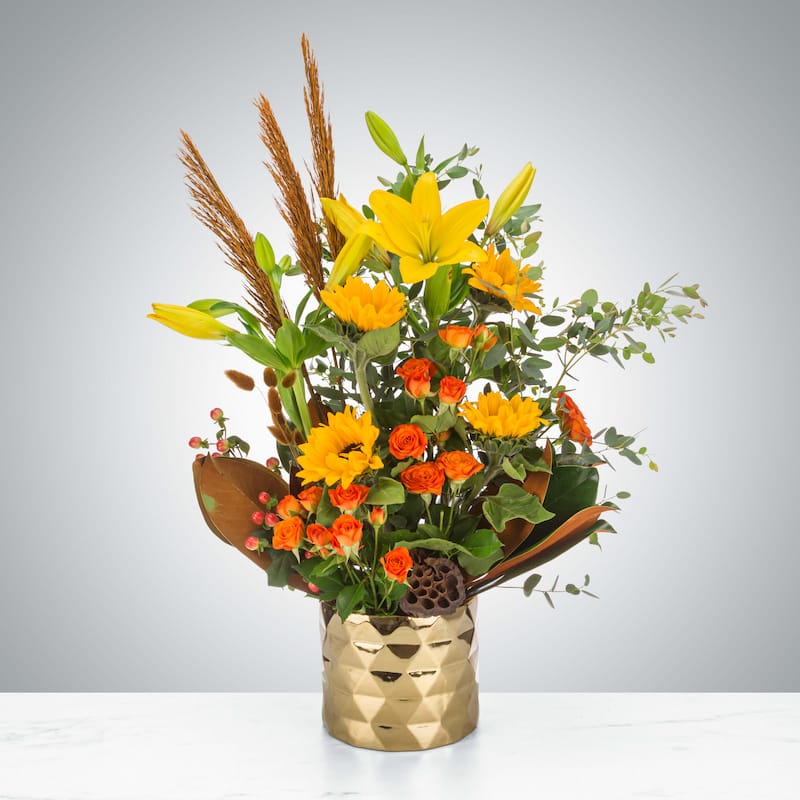 Tall, sculptural Thanksgiving centerpiece featuring golden yellow, russet, and amber blooms in a vertical arrangement for Naples holiday hosting.