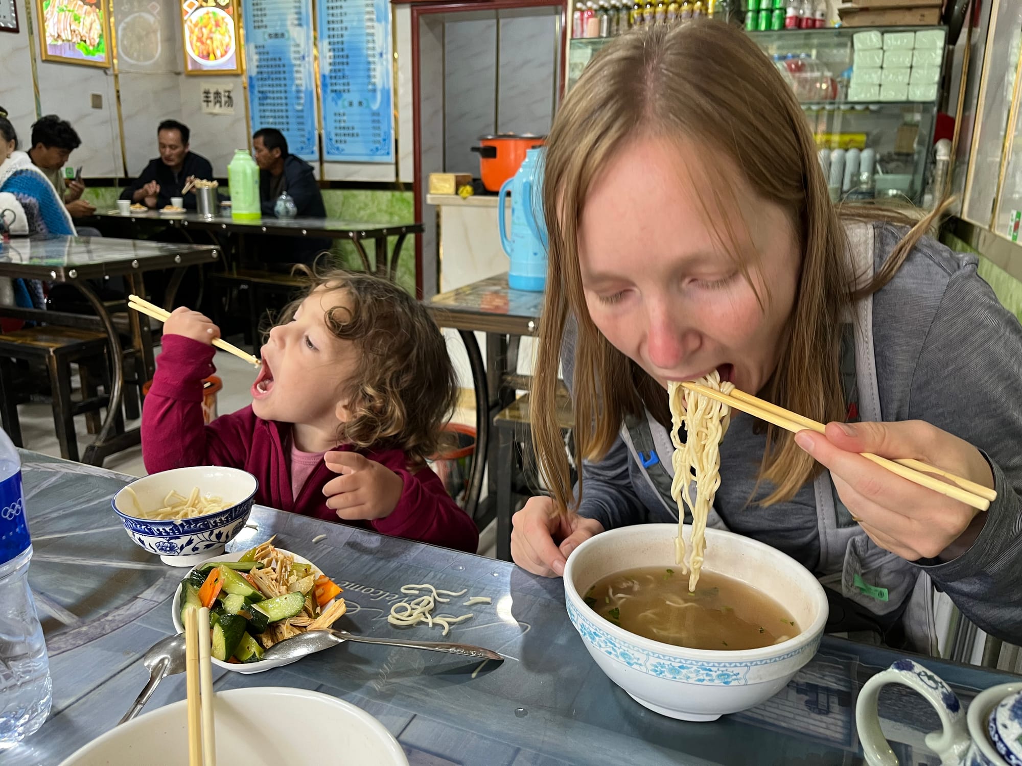 Toddler eating noodles with chopsticks at a restaurant in China
