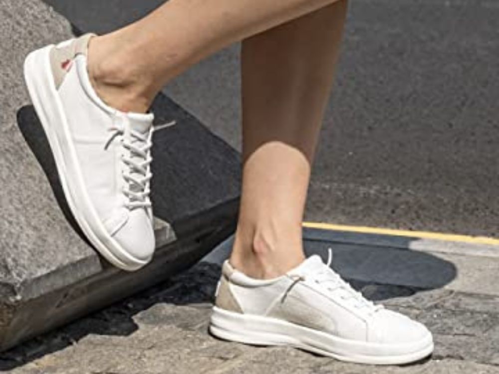 Person wearing white Hey Dude shoes with one foot back on a ledge.