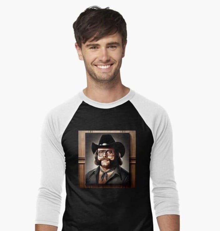 Buck "Sagebrush" Thompson wearing a black and white raglan shirt with a framed portrait graphic of a cowboy wrestler on the chest.