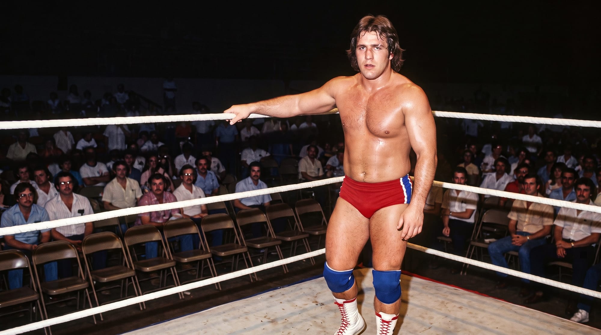Rocket Roger Rush stands in the corner of a Gulf Coast ring in red trunks and blue kneepads, one arm hooked over the top rope, in front of a Houston crowd on folding chairs
