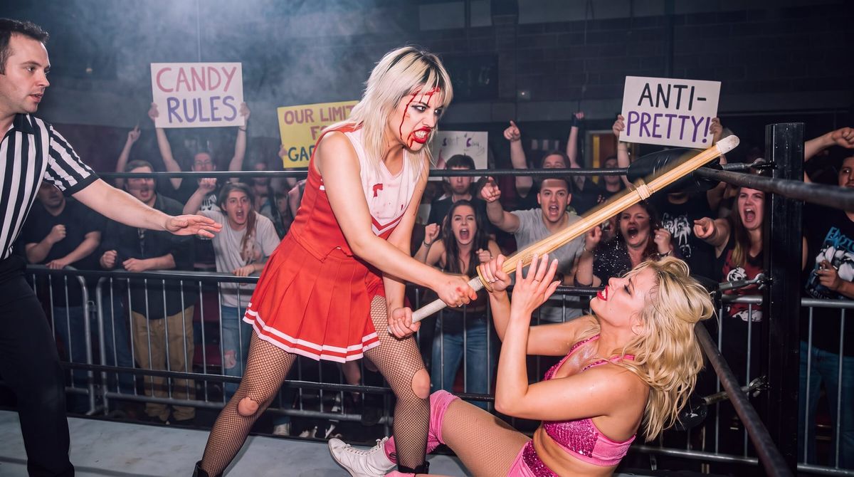 Women's hardcore wrestling, 1992: Trash Candy, bleeding from the hairline, drives a kendo stick down on a blonde opponent trapped in the corner as the crowd screams.