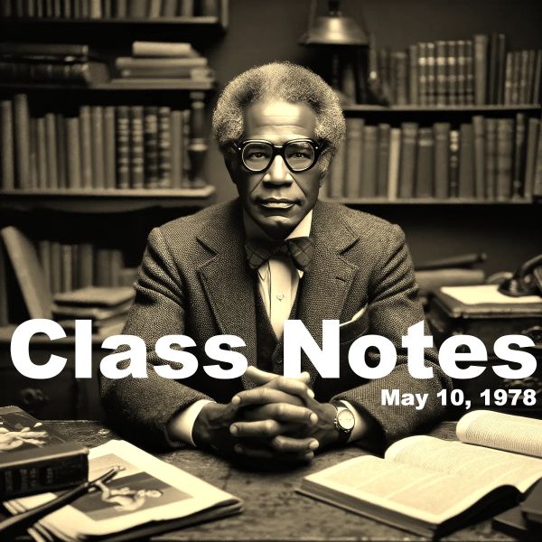 Man in glasses and suit seated at desk with books and papers, library shelves behind him, black and white photo from 1978.