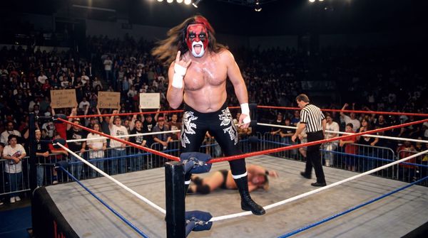 Scott Darkness on the ropes in a ring corner, making the heavy metal horns at a booing arena crowd while his opponent lies on the canvas.