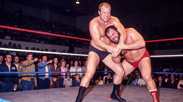 Wendell Briggs holds a bearded opponent in red trunks in a side headlock in front of a packed civic auditorium crowd, 1978.