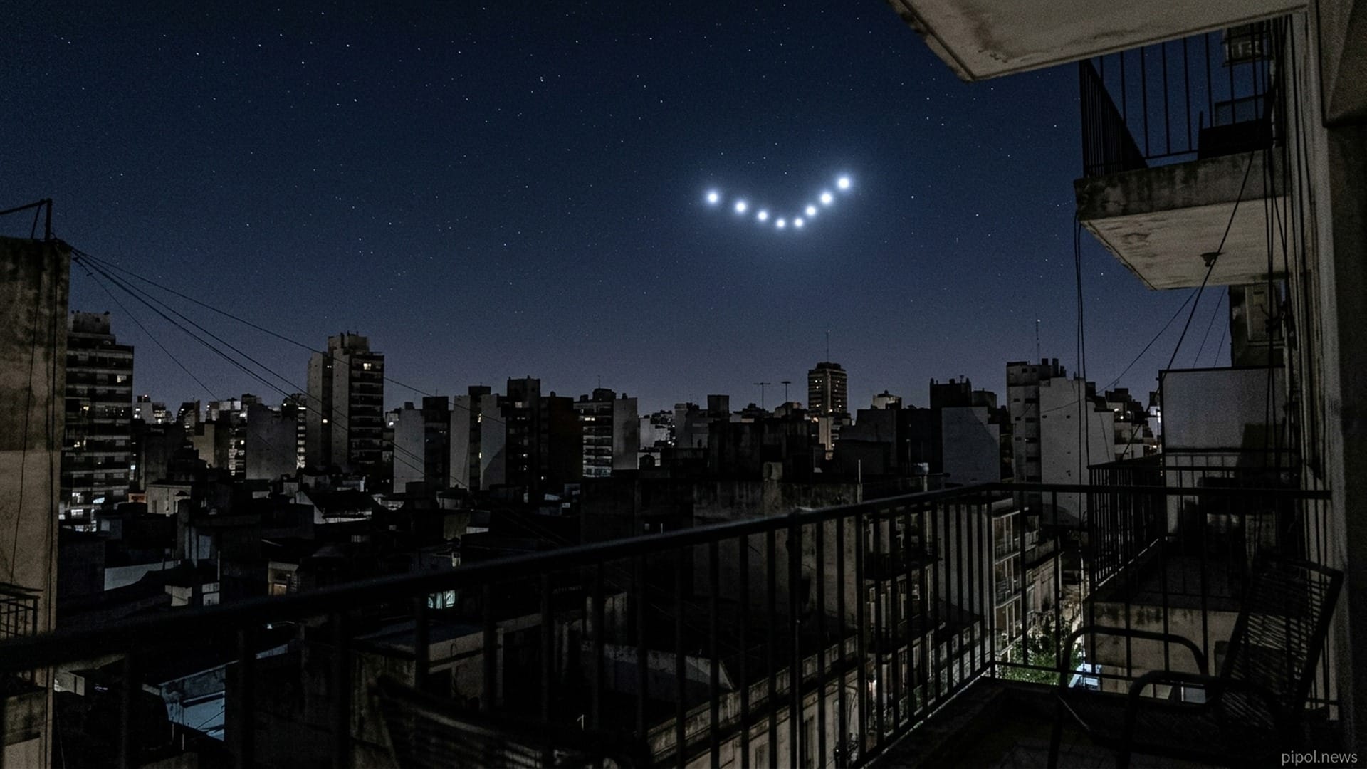 Vista en contrapicado desde un balcón en Buenos Aires hacia el cielo nocturno despejado con una formación luminosa en V