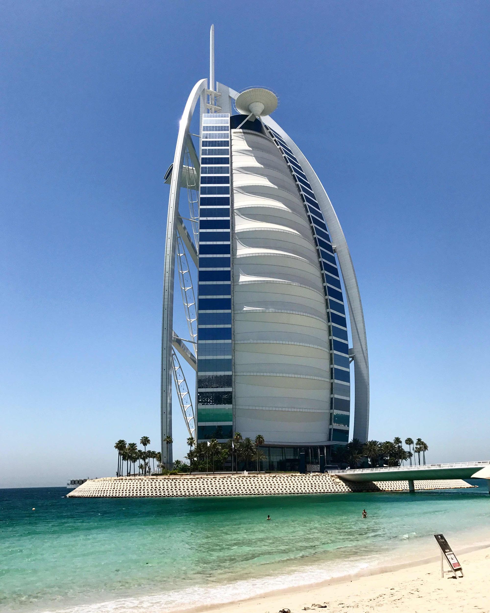 El hotel Burj Al Arab de Dubái, con su silueta blanca en forma de vela sobre el mar, visto desde la playa de arena.