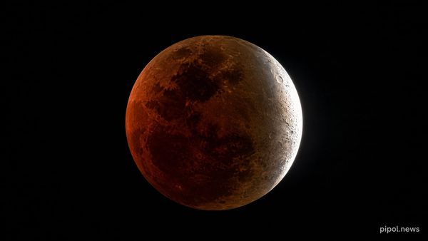 La Luna durante un eclipse parcial profundo: casi todo el disco teñido de cobre rojizo y un filo del borde derecho todavía iluminado en blanco.