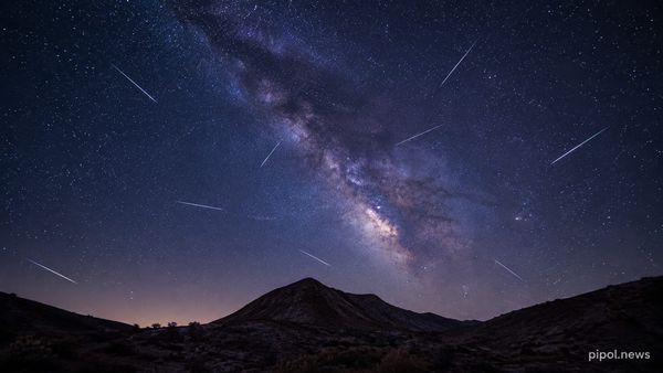 Cielo nocturno con la Vía Láctea en diagonal y una decena de meteoros cruzando en trazos finos sobre la silueta oscura de un cerro.