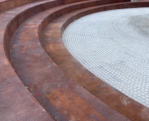 Del muro de contención al anfiteatro de hormigón rojizo terracota que sutura el desnivel entre la calle y el nuevo plano público