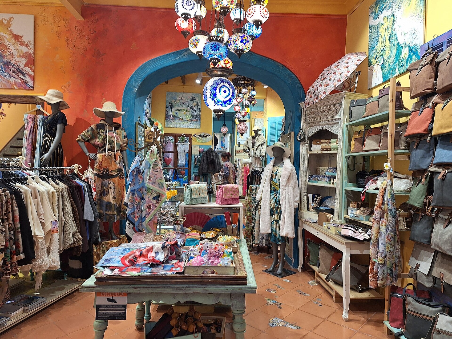 Interior of a specialty boutique with clothing racks, scarves, handbags and mannequins as a shopper browses at the back