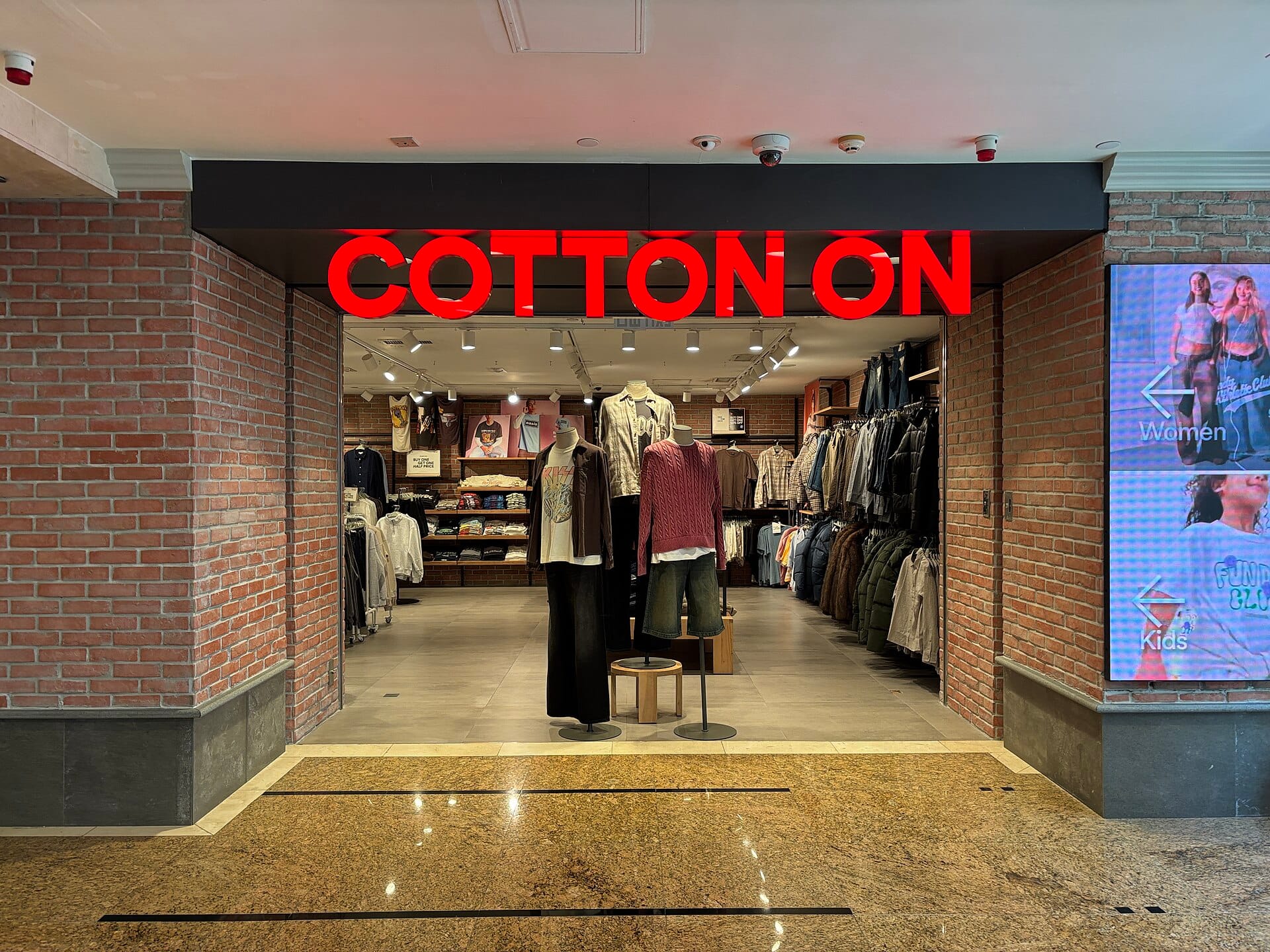 Open clothing store entrance in a mall with mannequins and window displays facing passing shoppers.