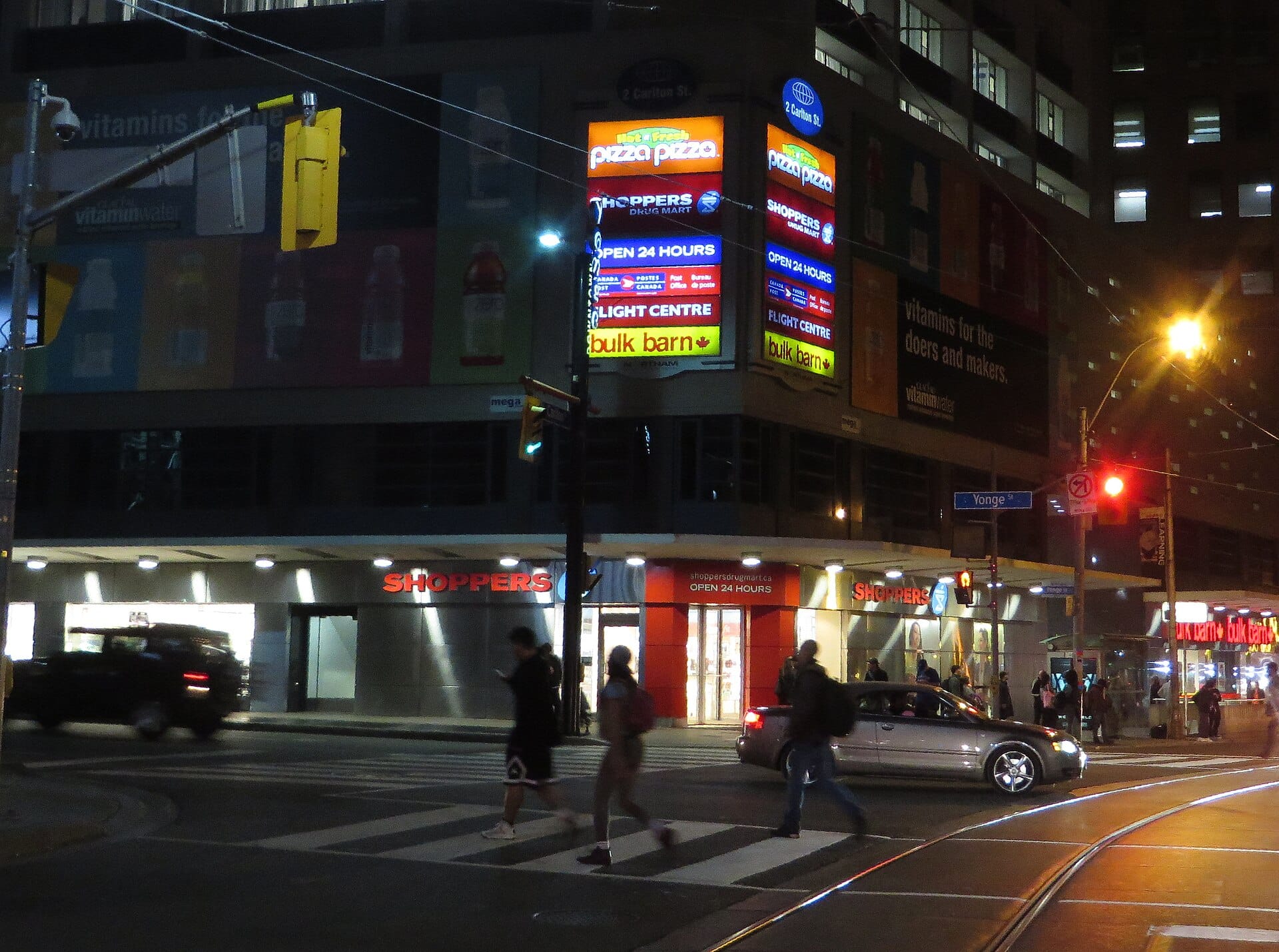 Pedestrians crossing a busy downtown city street lined with shops
