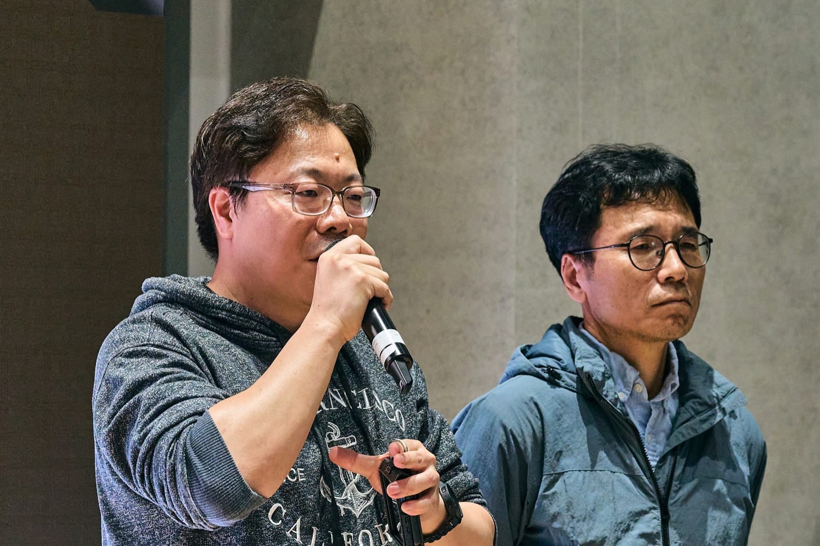 Team Dongbyeongsangryeon on stage, one member at the microphone introducing HubTrace while the other listens