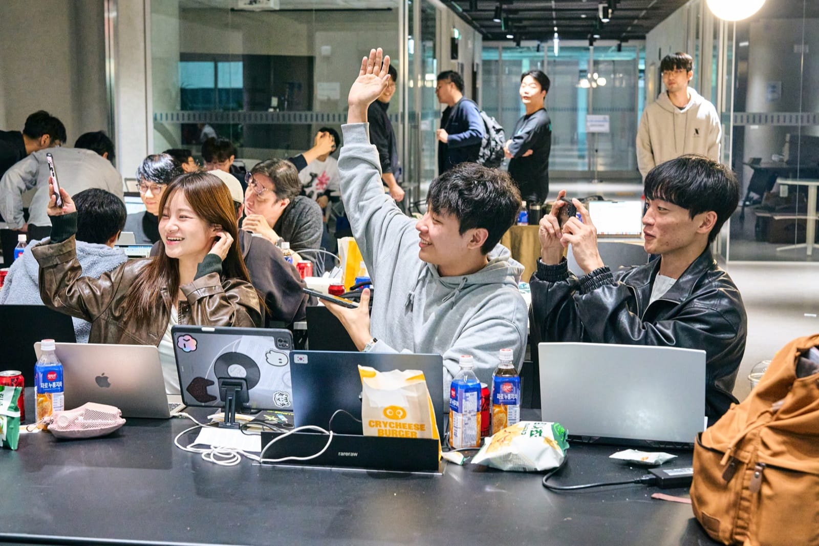 Participants at their laptops reacting to a result on the screen, one with a hand in the air and another filming it on a phone