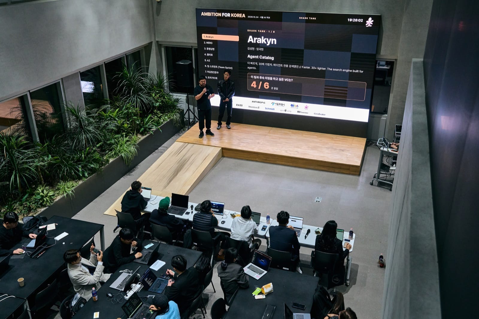 The Shark Tank stage seen from above, a finalist pitching under the LED wall with the audience seated below