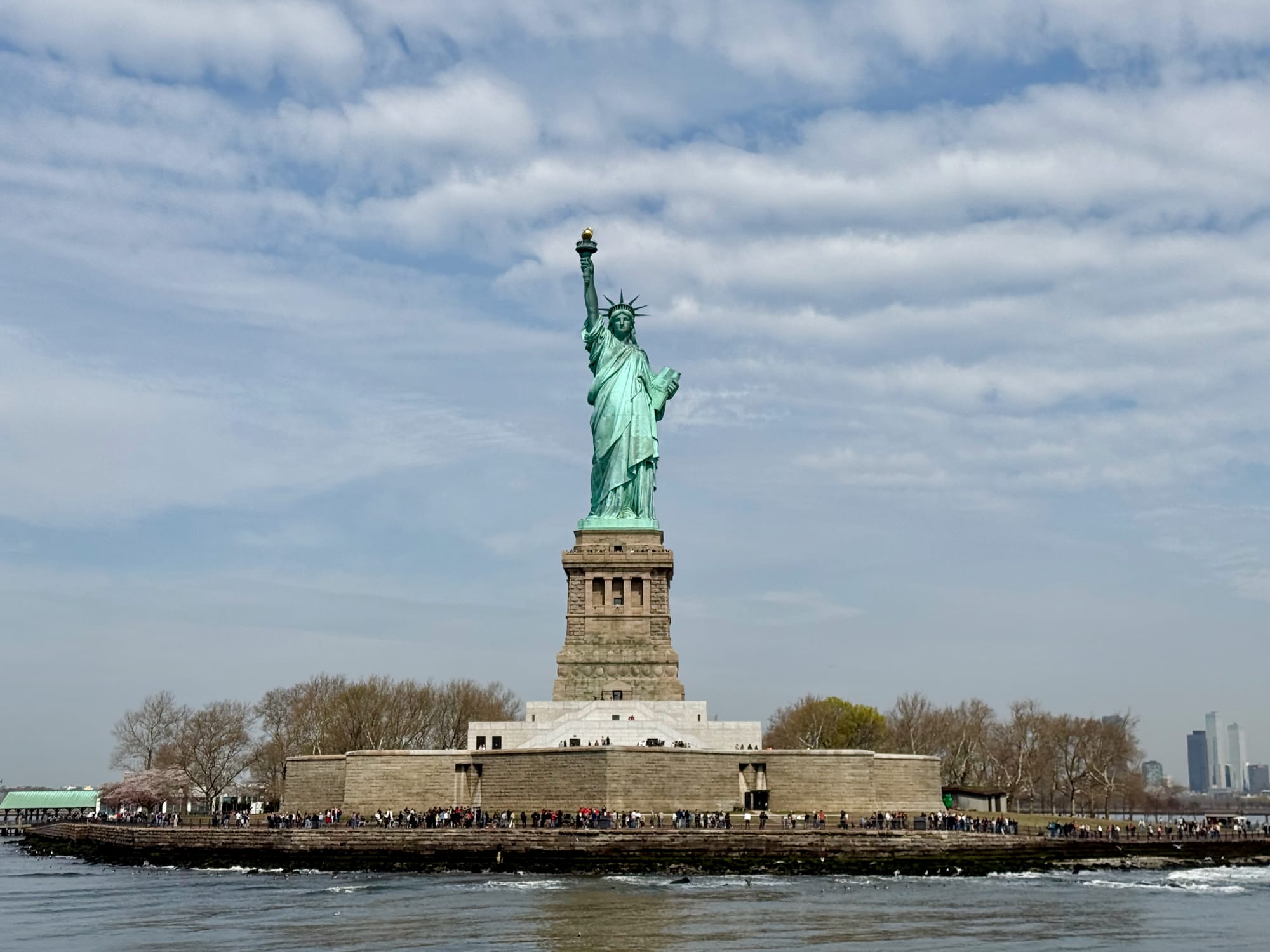 The Statue of Liberty on Liberty Island, seen from the water on a partly cloudy spring day during our New York City family trip