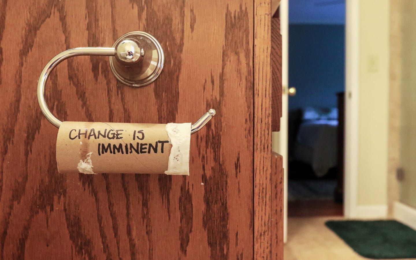 An empty toilet paper roll with ‘CHANGE IS IMMINENT’ written on it, humorously taped to a bathroom wall-mounted holder.