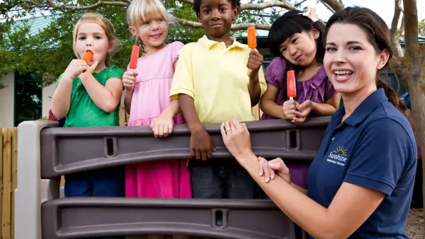photo of woman in a Sunshine Residential Homes polo shirt with a group of kids on a playground eating popsicles