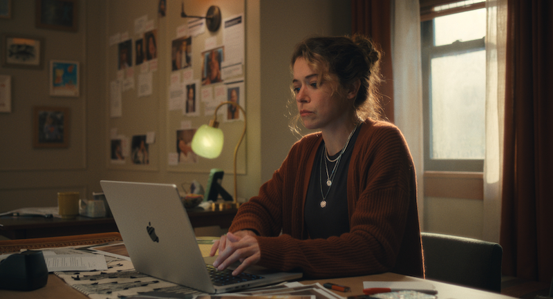 Tatiana Maslany as Paula in "Maximum Pleasure Guaranteed," sitting at a table and working on a laptop computer.