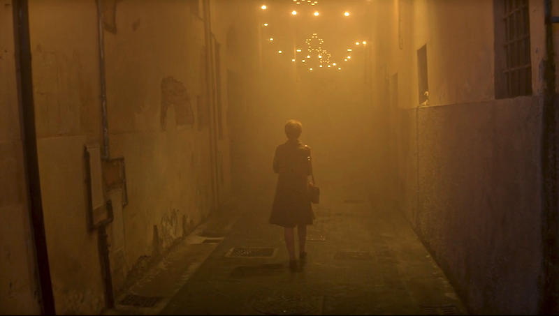 Lenu walks down a hazy yellow alleyway strung with twinkle lights and stars.