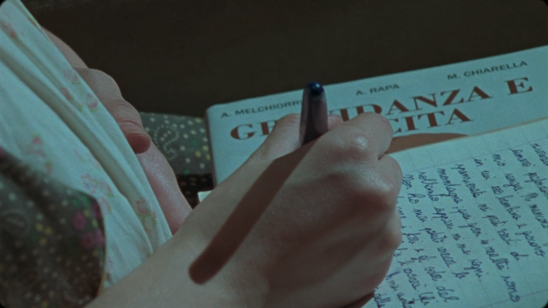 Pregnant Lila writes in her notebook. Only her belly, hand, and the notebook are visible.