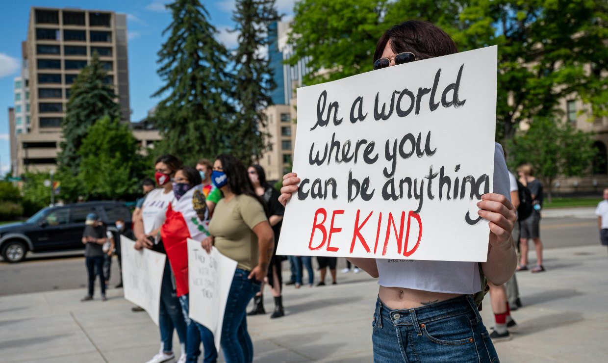 Protester holding sign that reads "in a world where you can be anything, be kind."