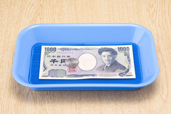 Eine Zahlschale mit einer 1000-Yen-Note und einer Münze im Wert von 100 Yen.