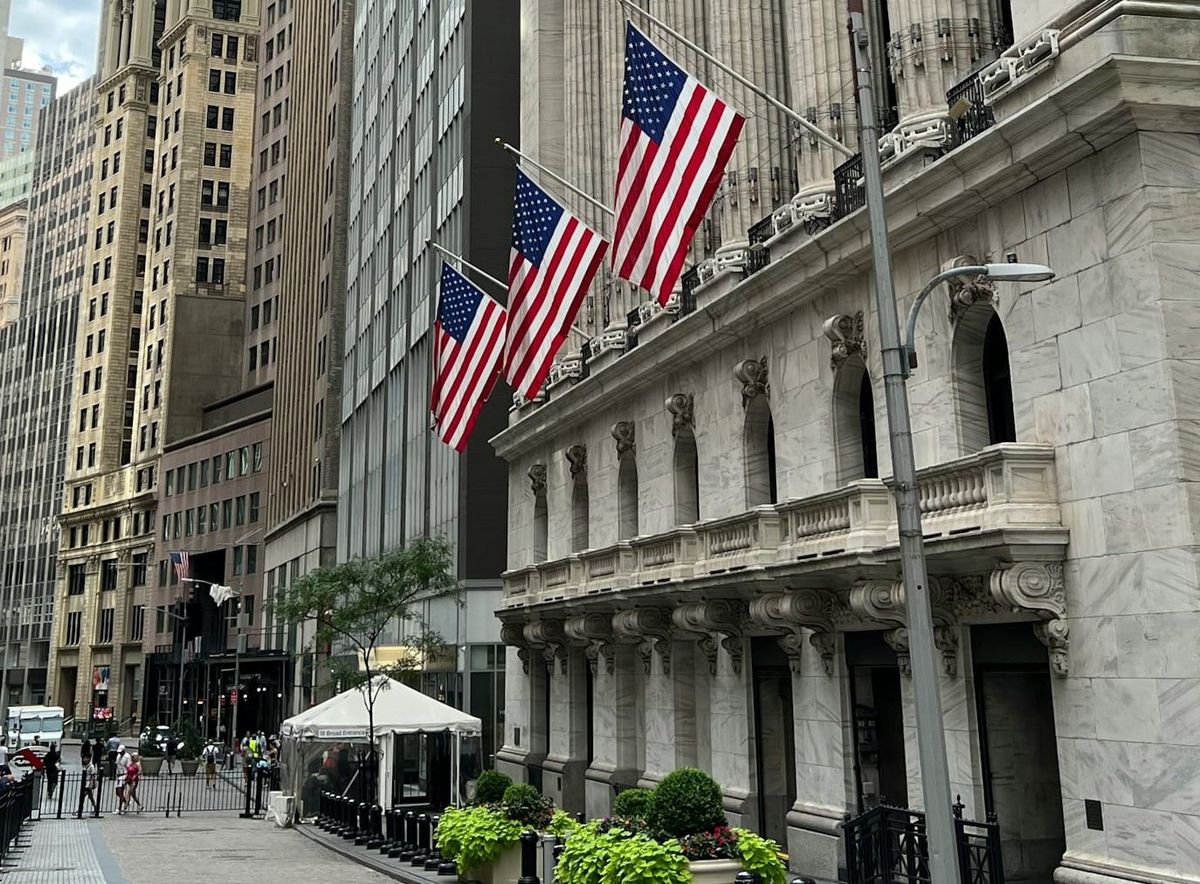 Wall Street financial district with bank buildings and stock market data displayed.