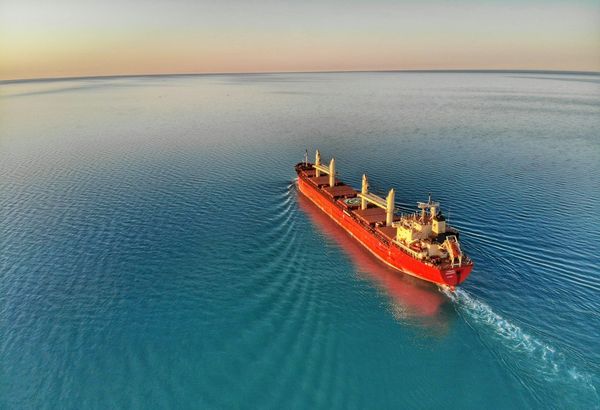 Oil tanker sailing representing LNG facility at Qatar’s Ras Laffan industrial hub with global gas price charts rising after supply disruption.