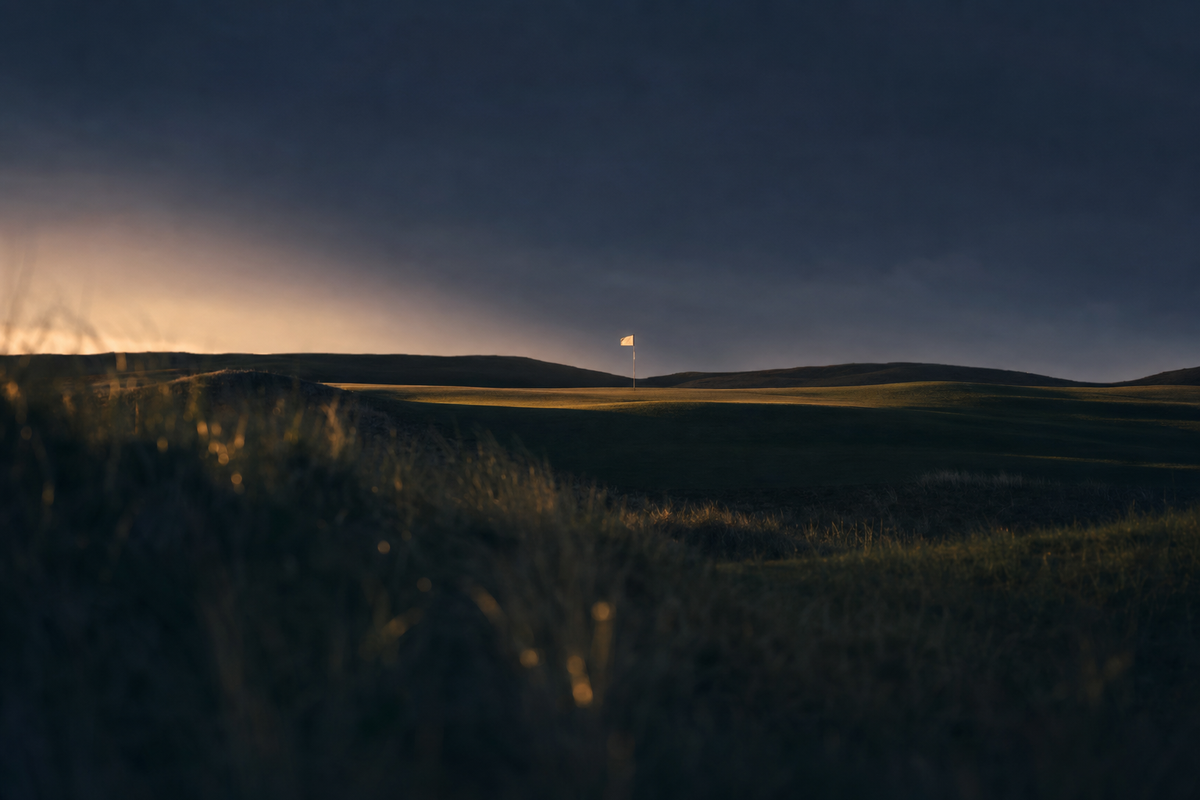 Empty manicured golf course at twilight with a single illuminated flagstick in the distance