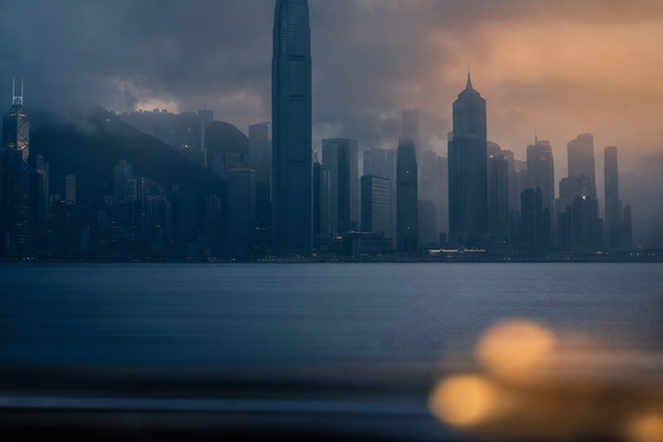 Hong Kong harbour skyline at dusk in soft fog with warm amber light pulse in the foreground