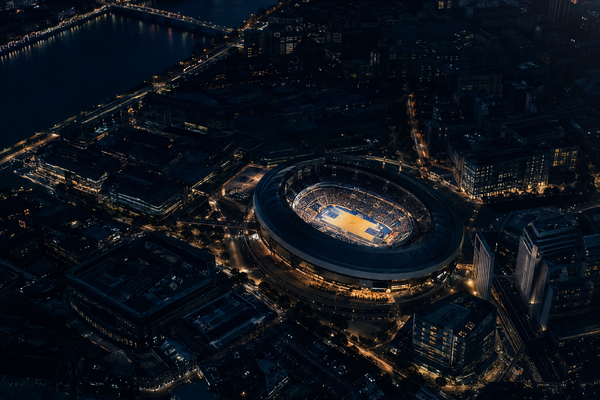 A lit basketball arena at night surrounded by a European city